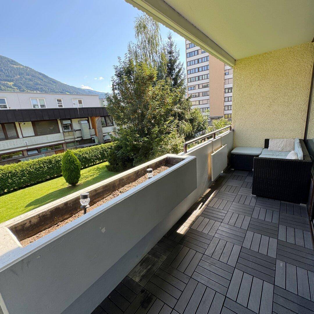 Sonniger Balkon mit modernen Bodenfliesen und bequemen Outdoor-Möbeln, umgeben von Grün.