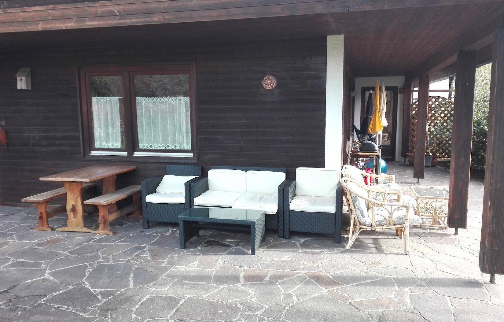 Überdachte Terrasse mit verschiedenen Sitzbereichen und einem Holztisch, ideal für Entspannung im Freien.