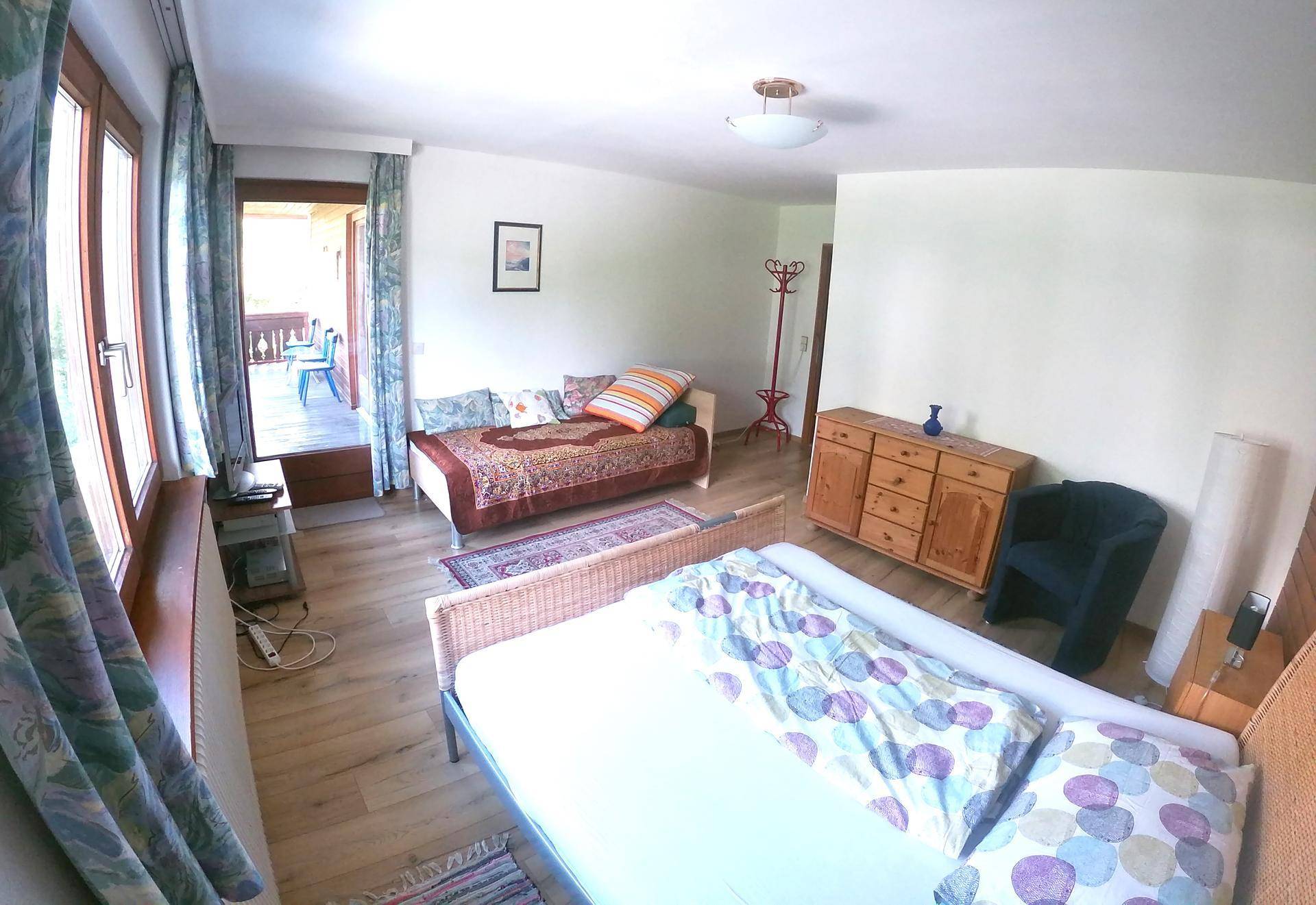 Helles Schlafzimmer mit Bett, Tagesbett und Zugang zu einem überdachten Balkon oder einer Loggia.