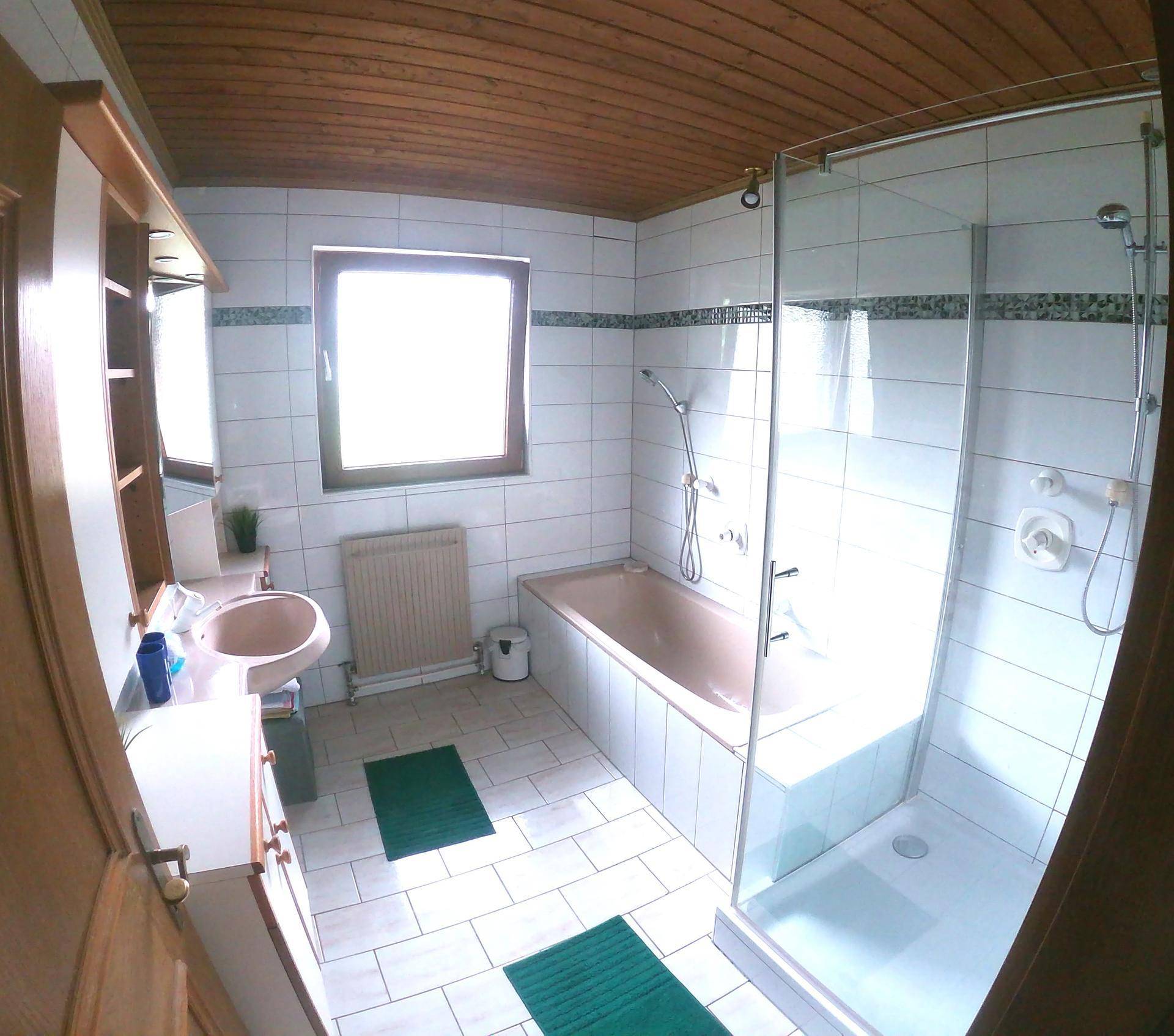 Helles Badezimmer mit Badewanne, Duschkabine, Fenster und Holzdecke in traditionellem Stil.