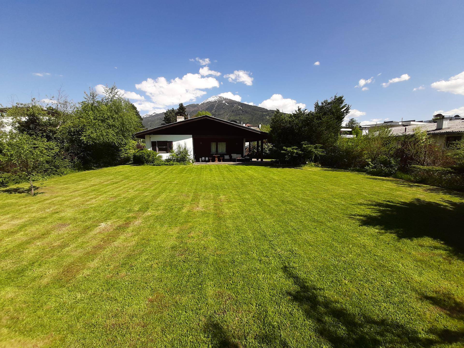 Weitläufiger grüner Garten mit einem charmanten Haus im Hintergrund und beeindruckendem Bergblick.