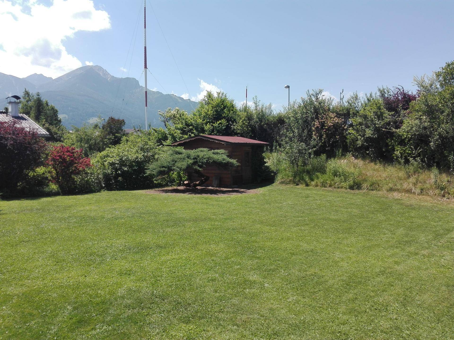 Gepflegter Garten mit Rasenfläche, einem Gartenhaus und Blick auf die umliegende Berglandschaft.