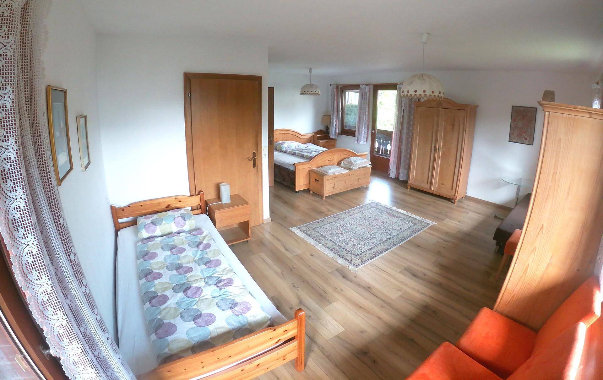 Geräumiges Schlafzimmer mit zwei Betten, Holzschrank und Blick auf den Balkon durch die Terrassentür.