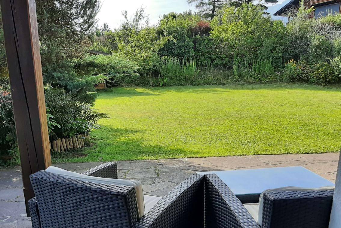 Blick von der Terrasse auf den weitläufigen grünen Garten mit Rasen und üppiger Bepflanzung.