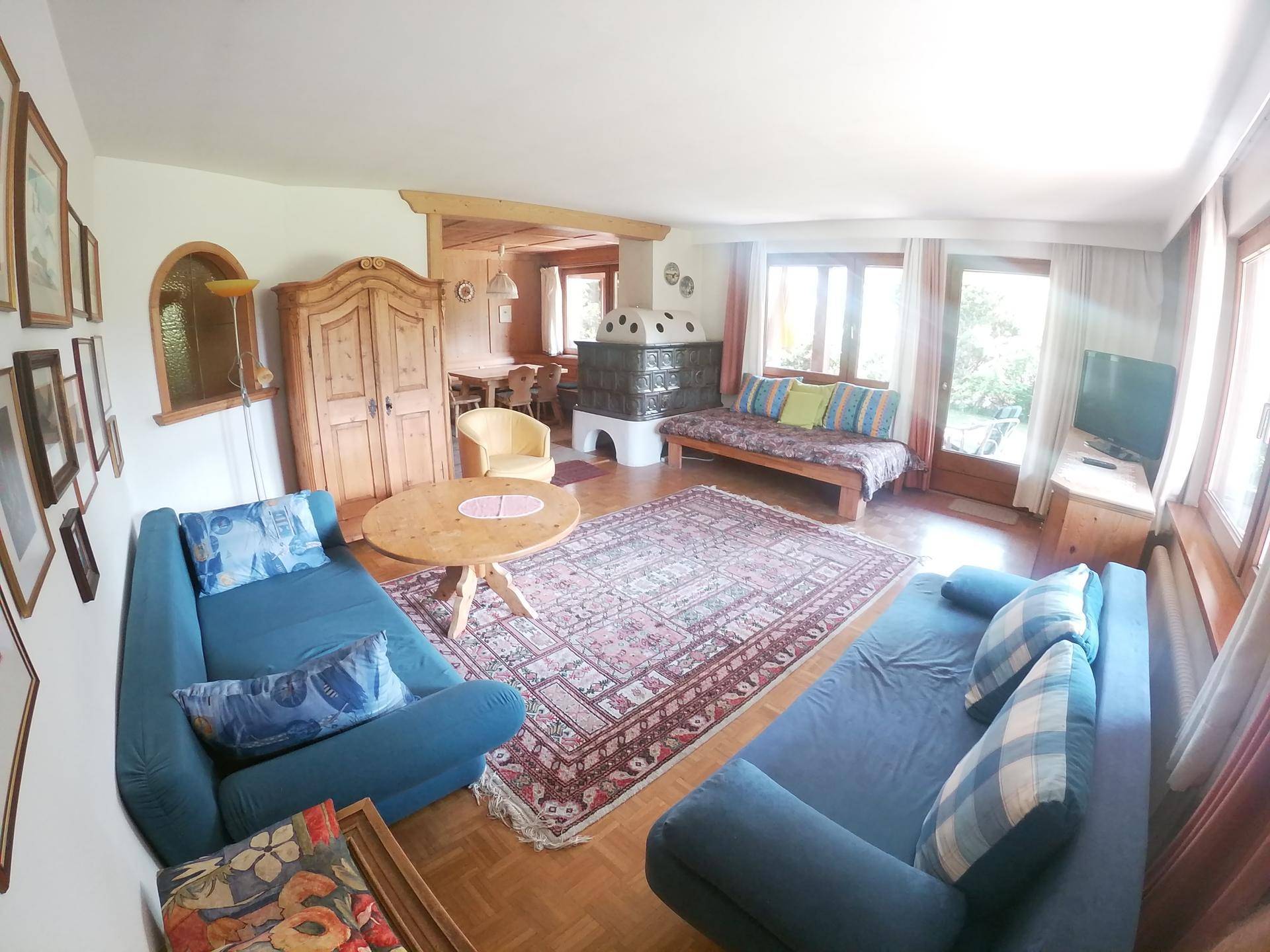 Geräumiges Wohnzimmer mit Kachelofen, bequemen Sofas und direktem Zugang zum Gartenbereich.