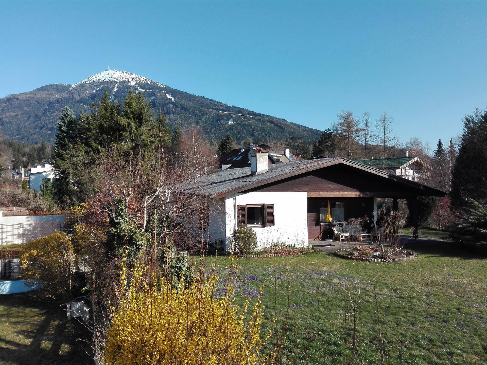Haus mit weitläufigem Garten und überdachter Terrasse, umgeben von Bäumen und schneebedeckten Bergen.