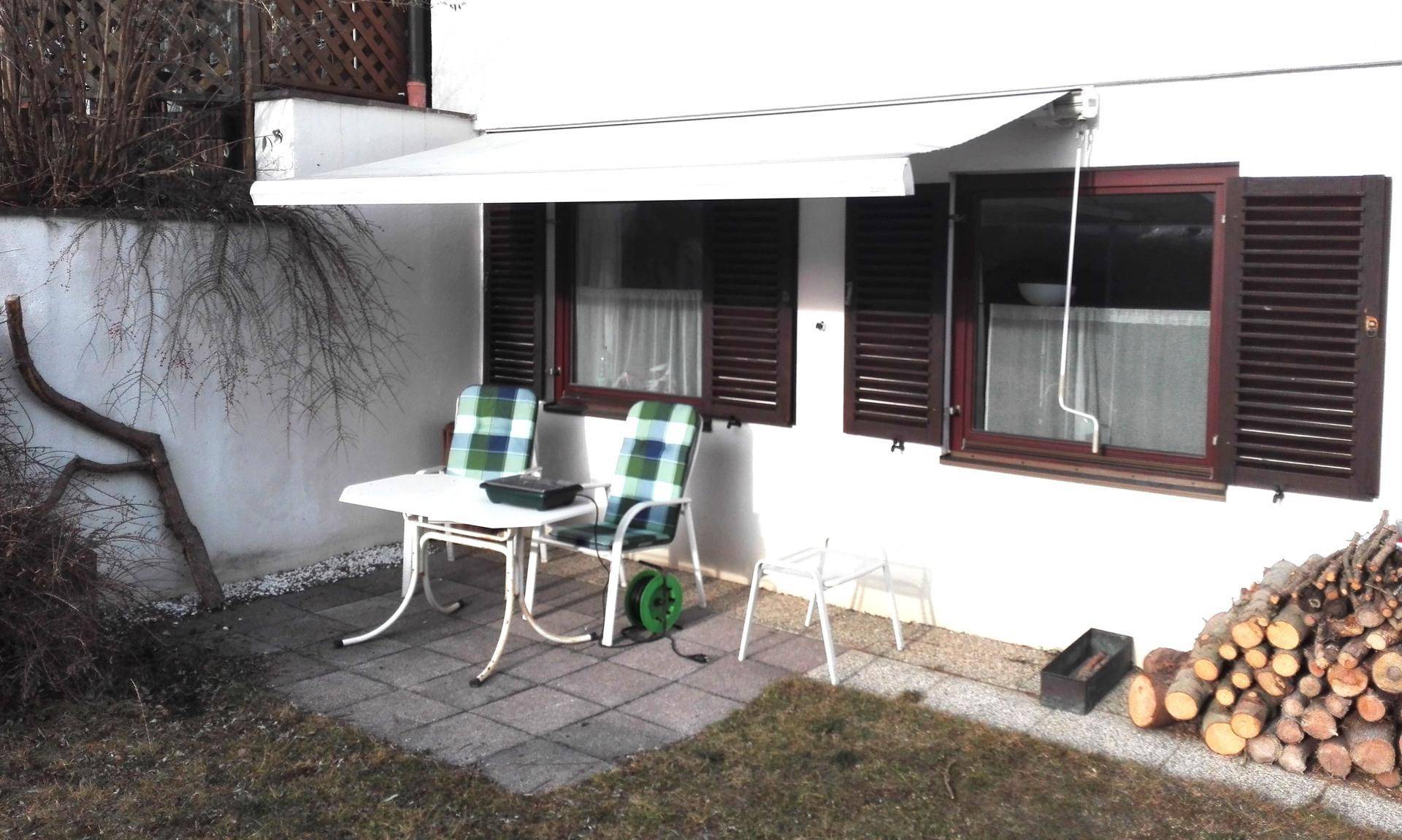 Gemütliche Terrasse mit Sitzgelegenheiten, Markise und Holzstapel im Freien.