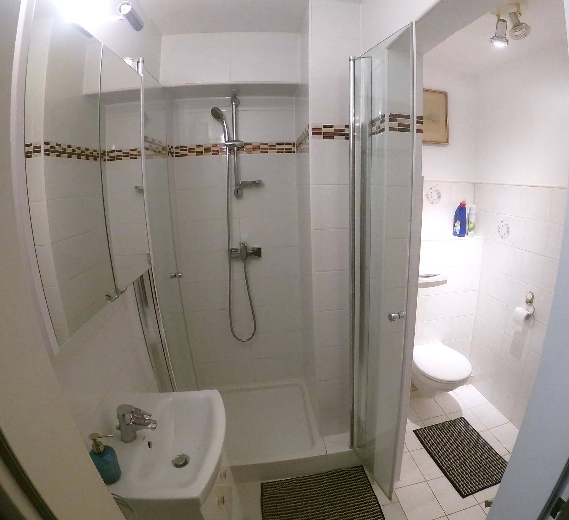 Helles Badezimmer mit Duschkabine, WC und weißen Fliesen.