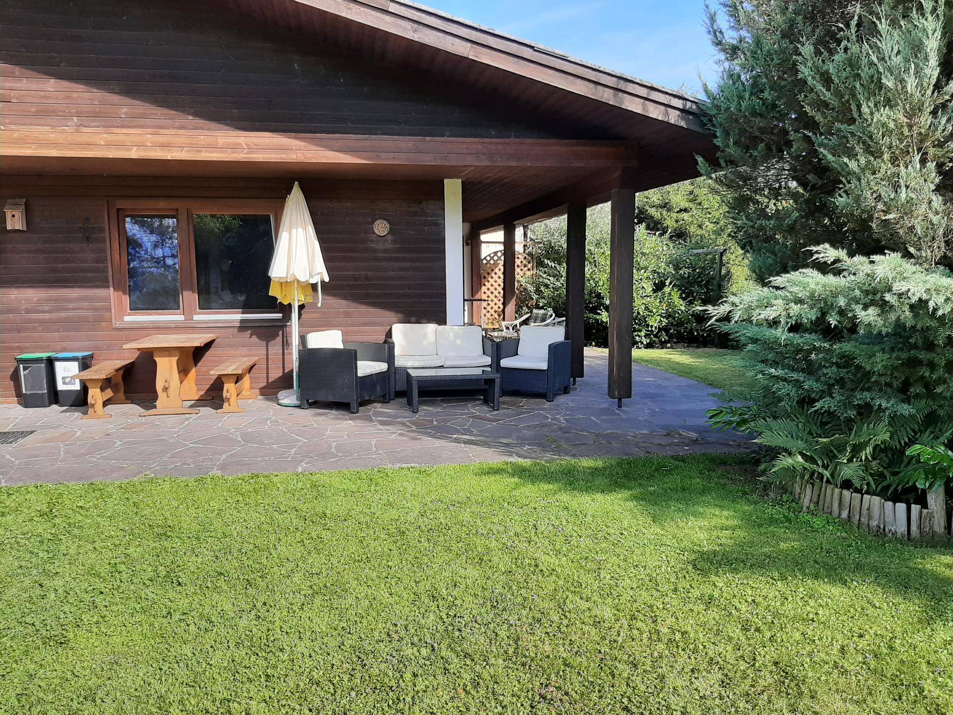 Große gepflasterte Terrasse mit modernen Gartenmöbeln und einem Holztisch, umgeben von Rasen.