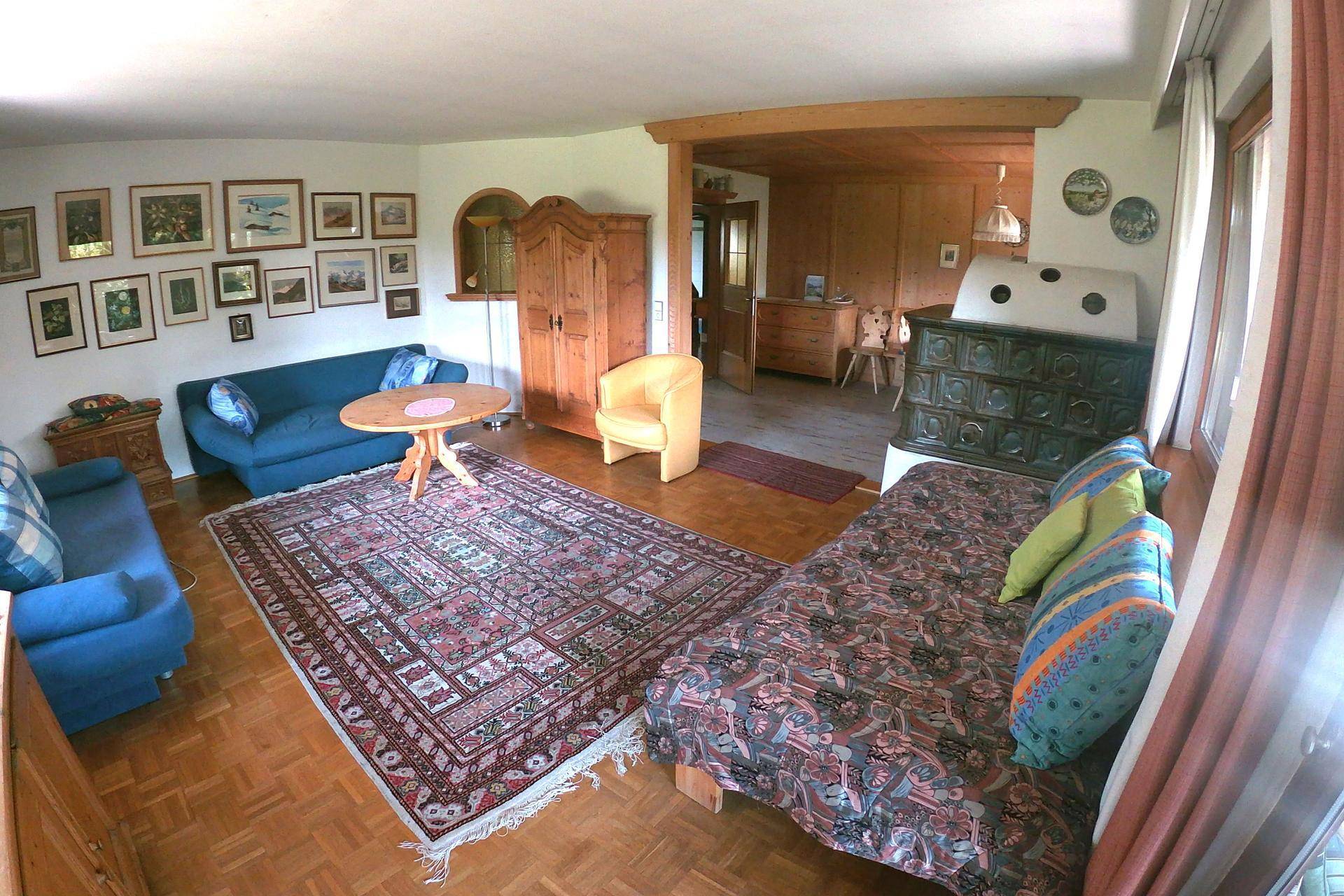 Traditionelles Wohnzimmer mit Kachelofen, blauen Sofas und Holzboden, reich verziert mit Bildern.