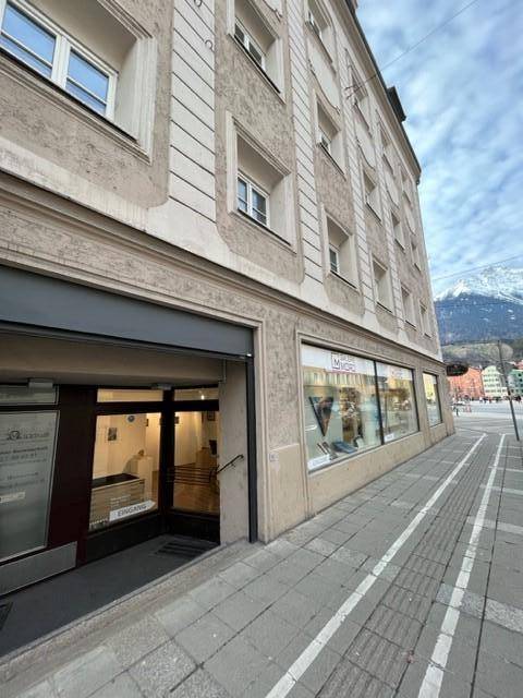 Weitläufige Ansicht der Gebäudefassade von der Straße mit Eingang, Schaufenstern und klarem Bergblick.