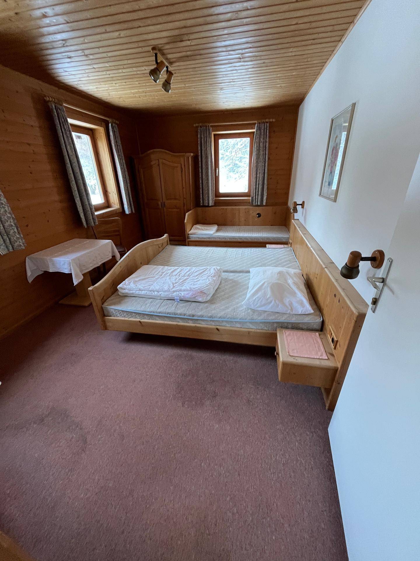 Helles Schlafzimmer mit Holzvertäfelung, zwei Einzelbetten und einem Kleiderschrank, mit Blick ins Grüne.