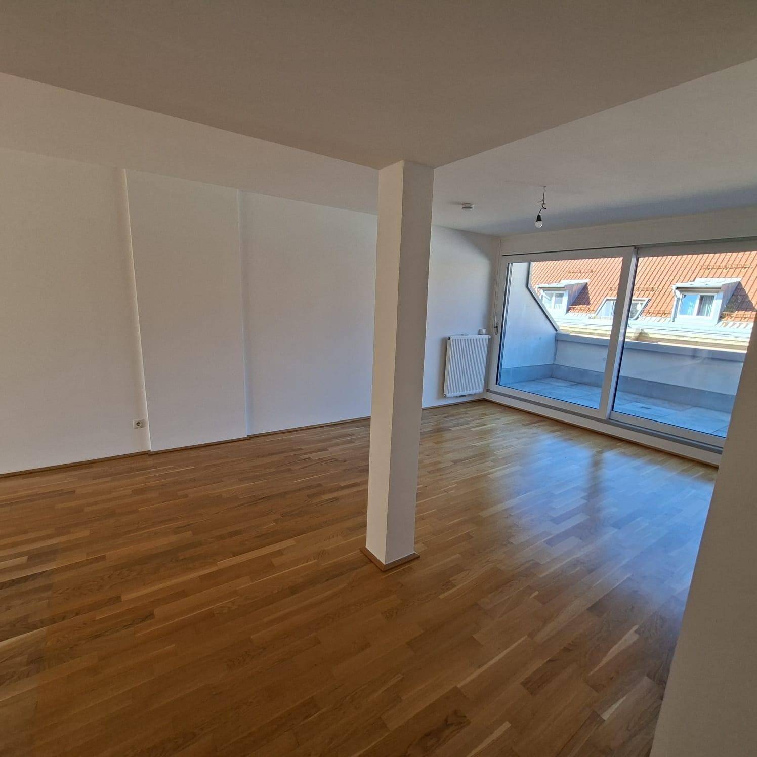 Geräumiges Wohnzimmer mit Parkettboden und Zugang zu einem Balkon oder einer Terrasse.