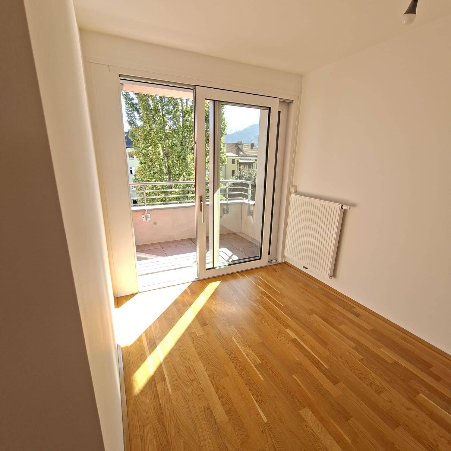 Schlafzimmer mit Parkettboden, Balkonzugang und Blick ins Grüne mit Bäumen.