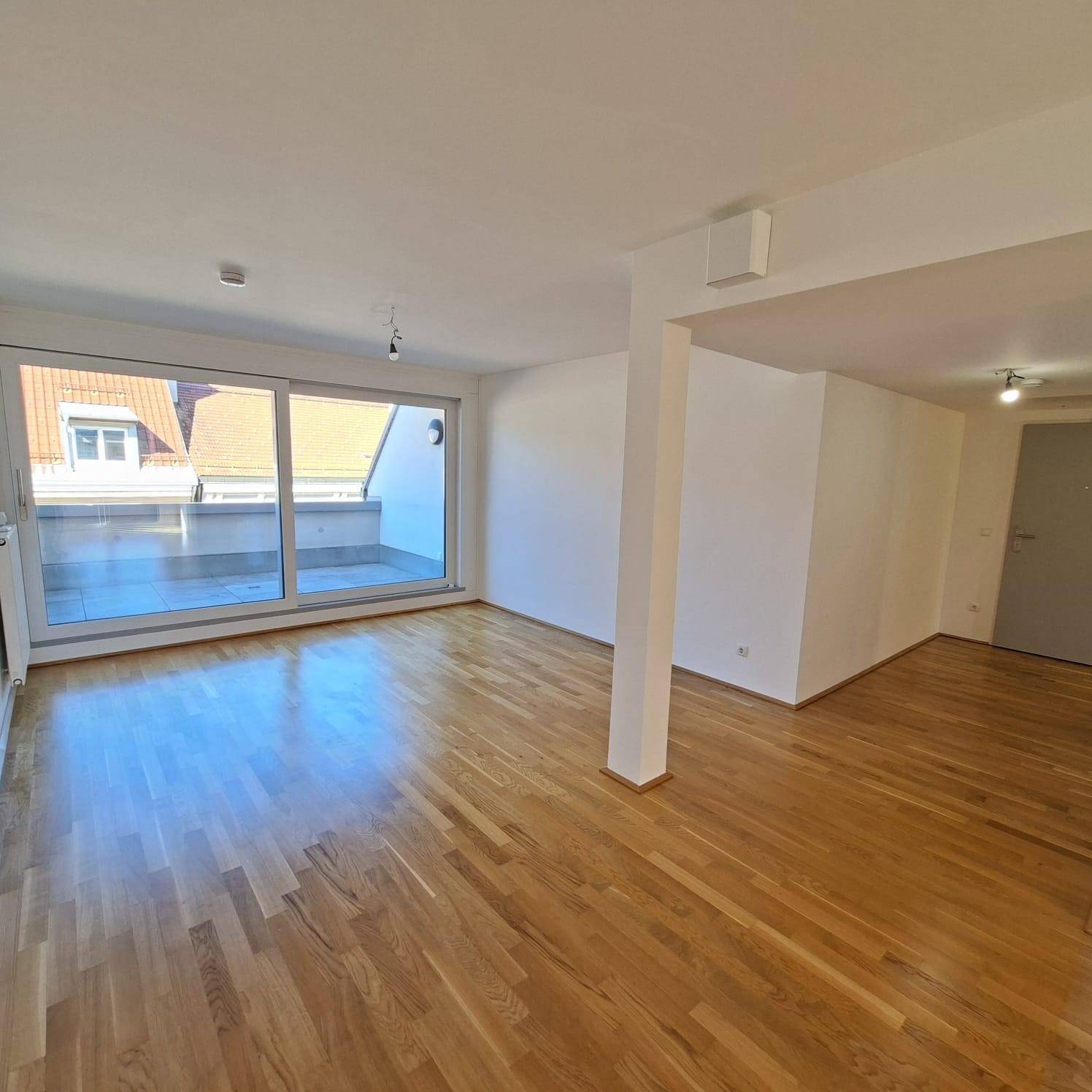 Heller Wohnbereich mit Holzparkett und breiter Schiebetür, die auf einen Außenbereich führt.