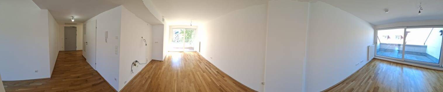 Weitläufiger Wohnbereich mit Parkettboden, hellem Ambiente und Zugang zu einem Außenbereich.