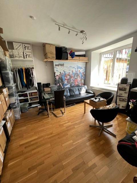 Wohnzimmer mit Holzfußboden, Sofa und Regalen voller Kartons, was auf eine Lagerfläche hindeutet.