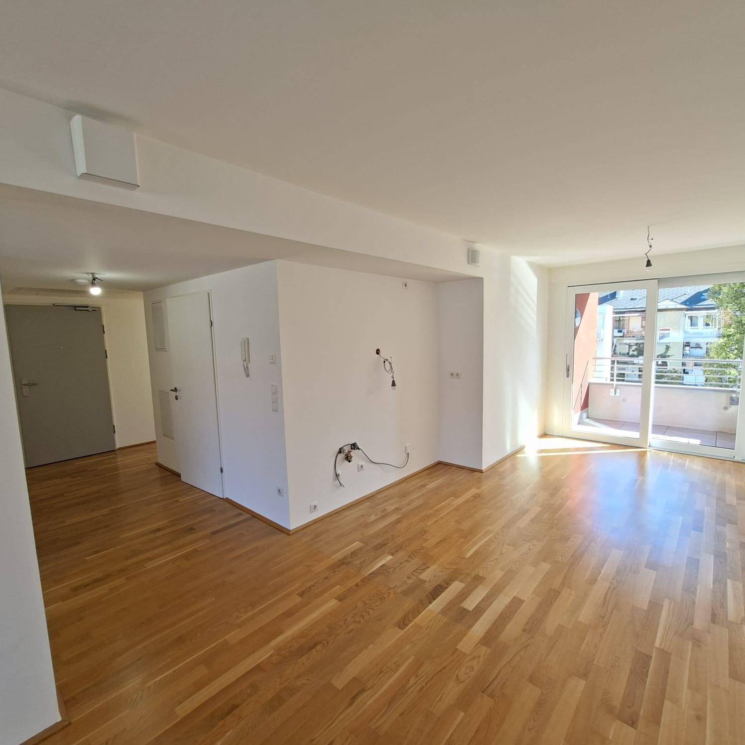 Offener Wohnbereich mit Parkettboden und Zugang zu einem sonnigen Balkon.