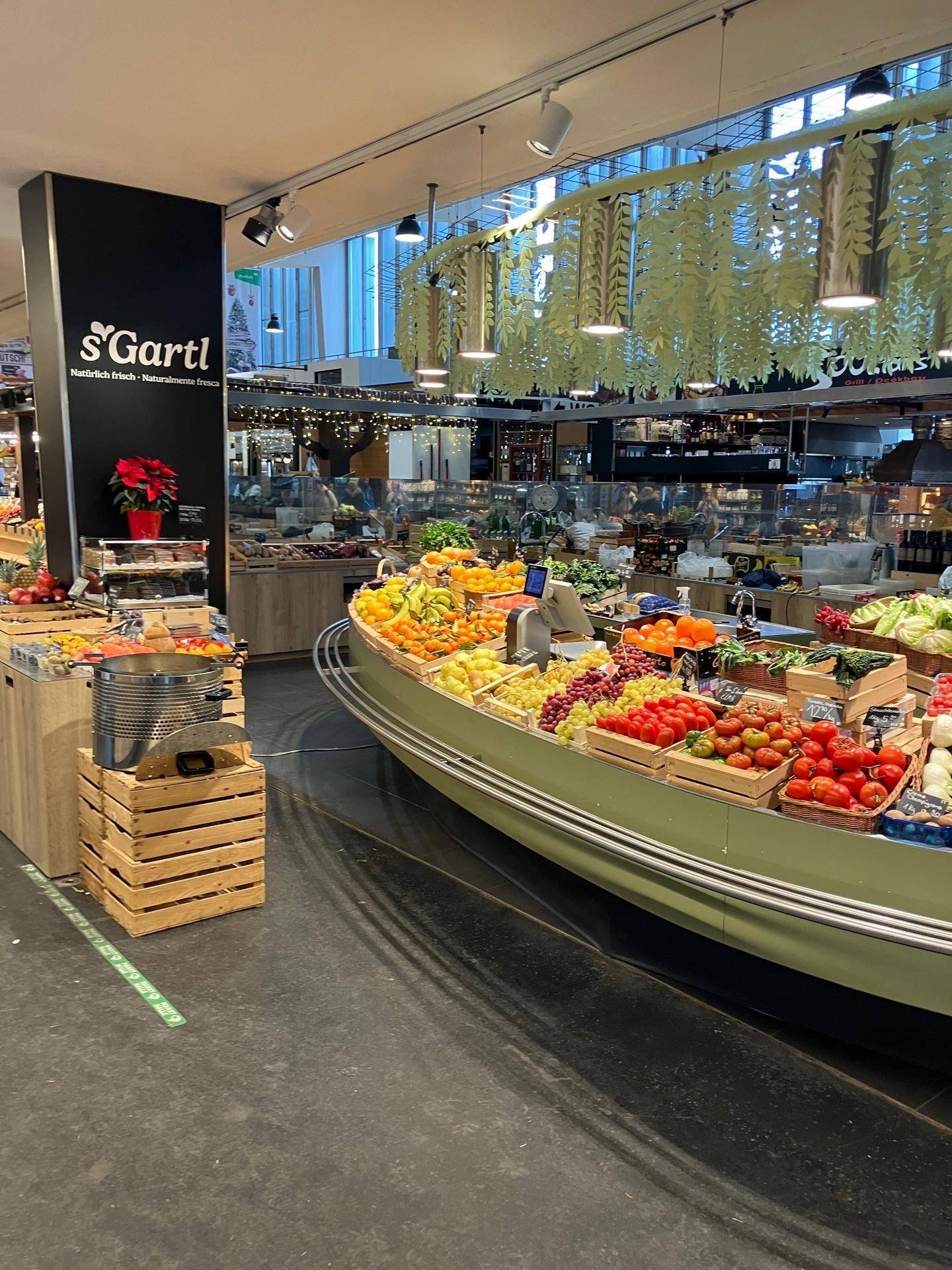Weitläufiger Verkaufsbereich in einer Markthalle mit einer reichhaltigen Auswahl an frischem Obst und Gemüse.