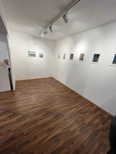 Heller Bereich des Gewerberaums mit Laminatboden, weißen Wänden und Kunstwerken, beleuchtet durch Spots.