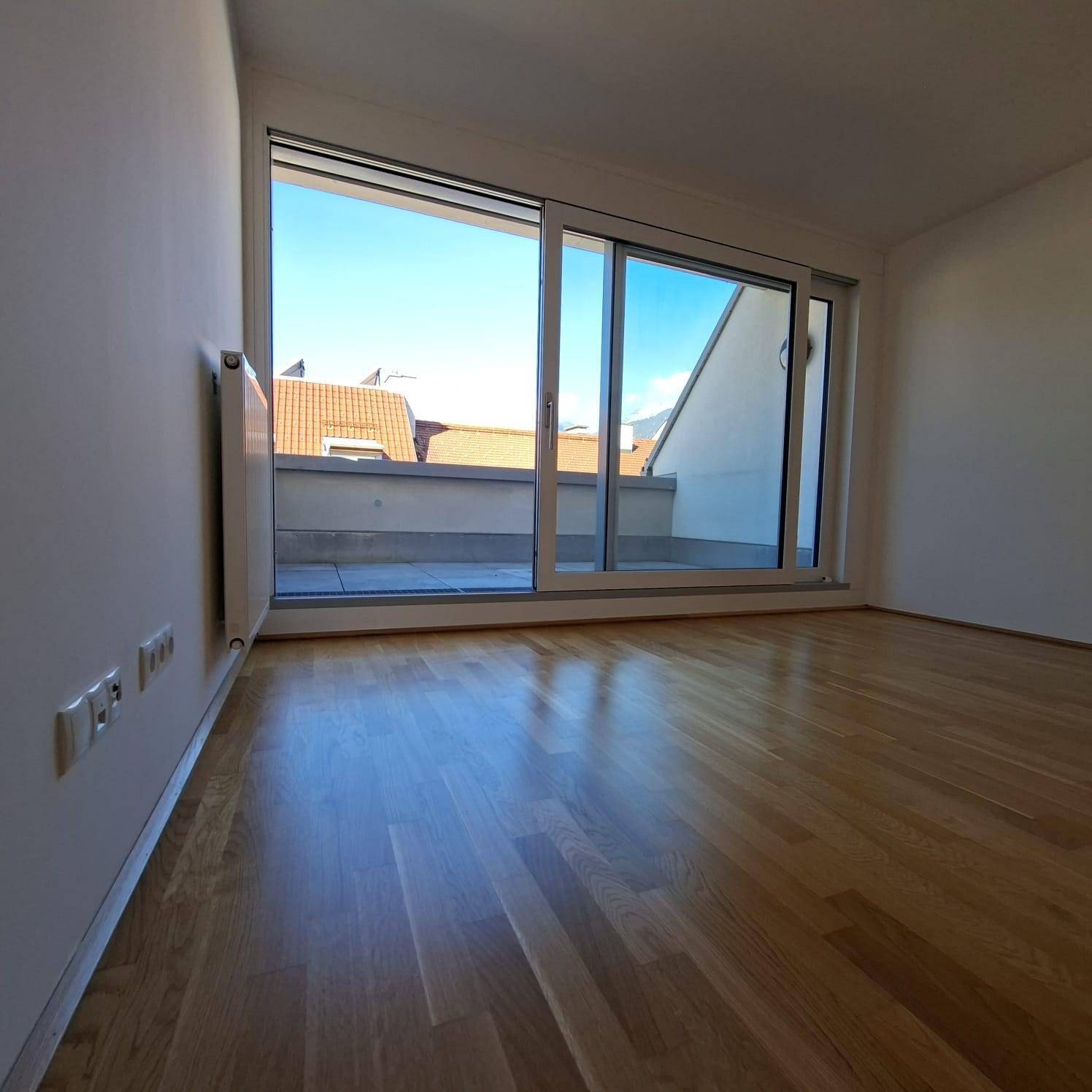 Helles Zimmer mit Parkettboden und großzügiger Schiebetür zu einem Außenbereich.