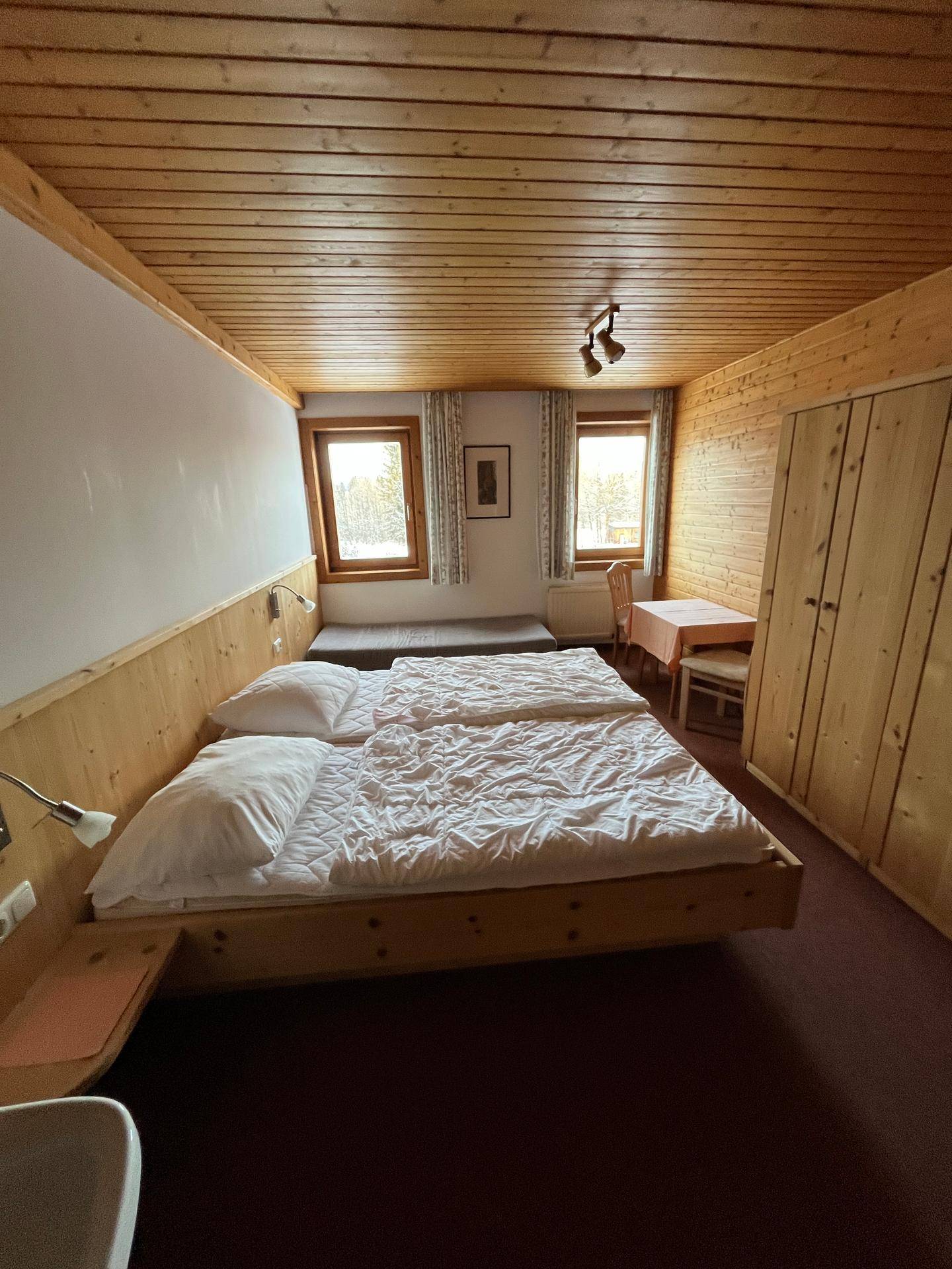Gemütliches Schlafzimmer mit Holzverkleidung an Wänden und Decke, ausgestattet mit zwei Betten und Fenstern.