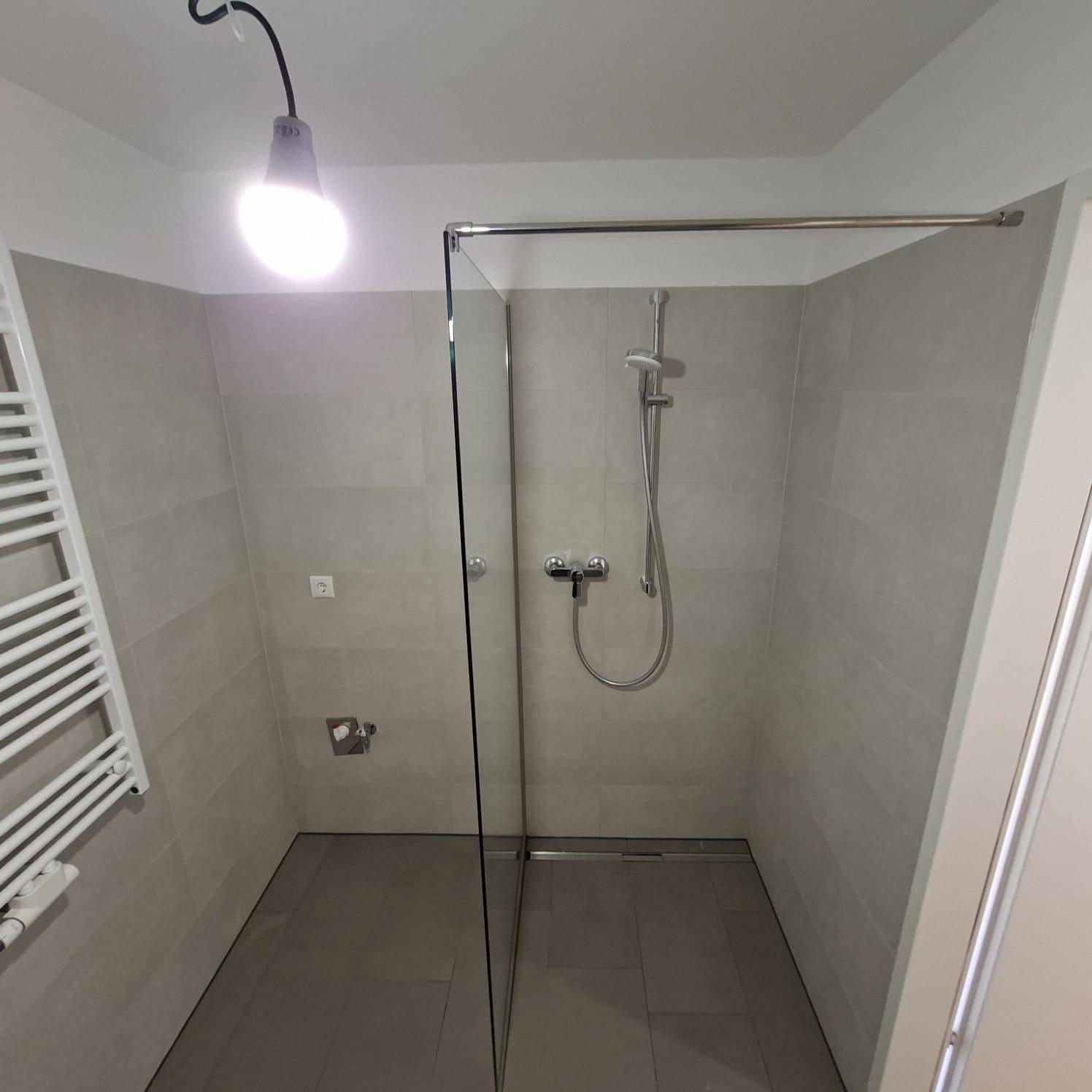 Modernes Badezimmer mit ebenerdiger Dusche und Glasabtrennung, ausgestattet mit Handtuchheizkörper.