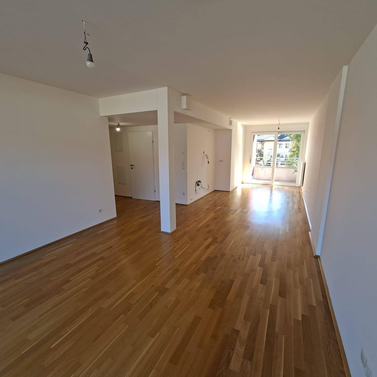 Langer, heller Wohnbereich mit Parkettboden und weitem Blick durch die Balkontür.