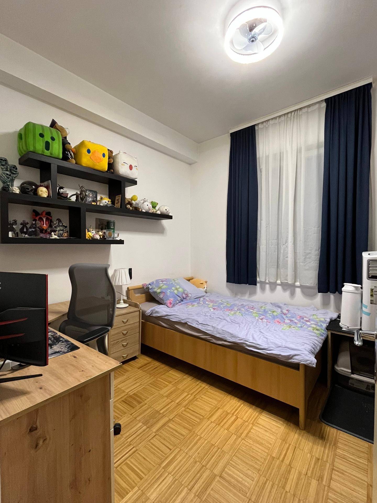 Helles Schlafzimmer mit Einzelbett, Holzparkett und einem Schreibtisch am Fenster.