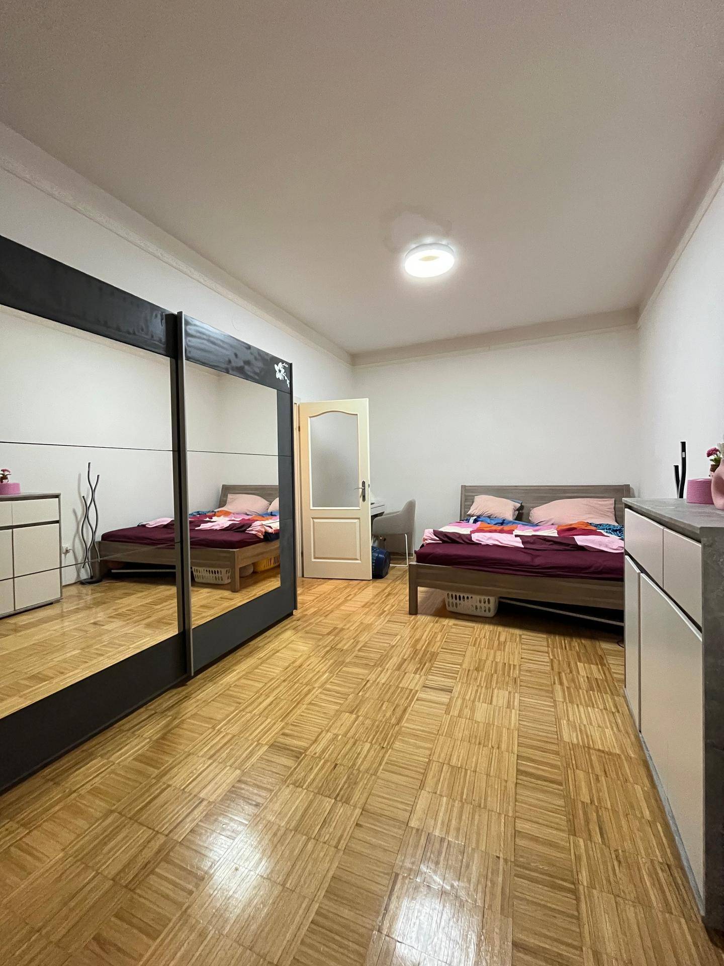 Geräumiges Schlafzimmer mit zwei Betten, großem Spiegelschrank und Parkettboden.