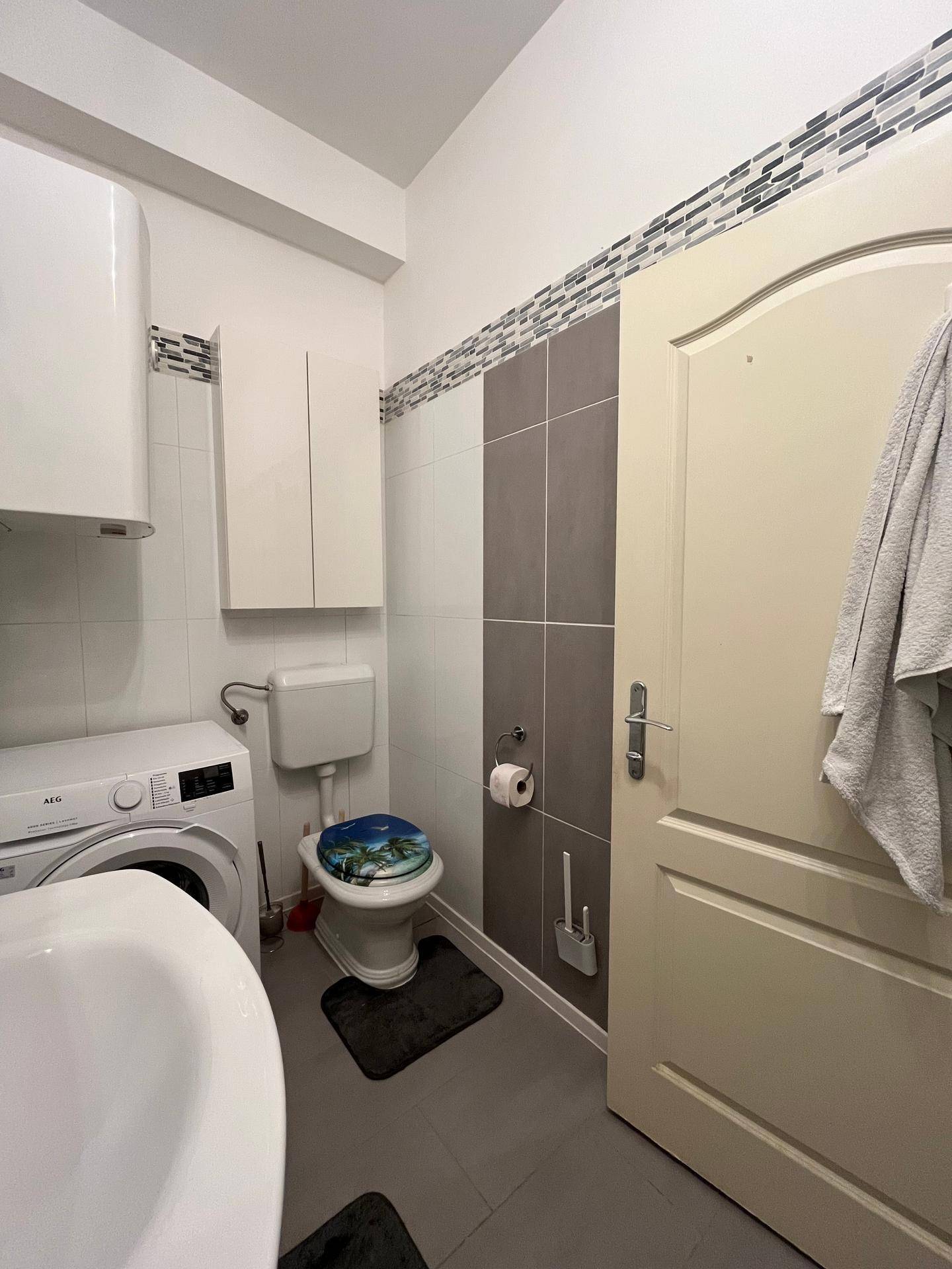 Badezimmer mit Toilette, Waschmaschine und modernen Fliesen an den Wänden.