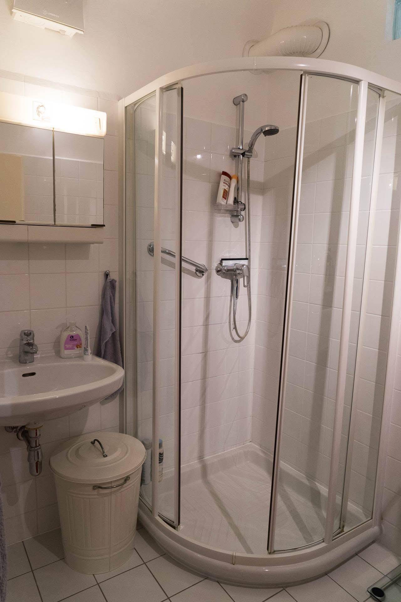 Badezimmer mit Eckdusche, Waschbecken und weißen Fliesen.