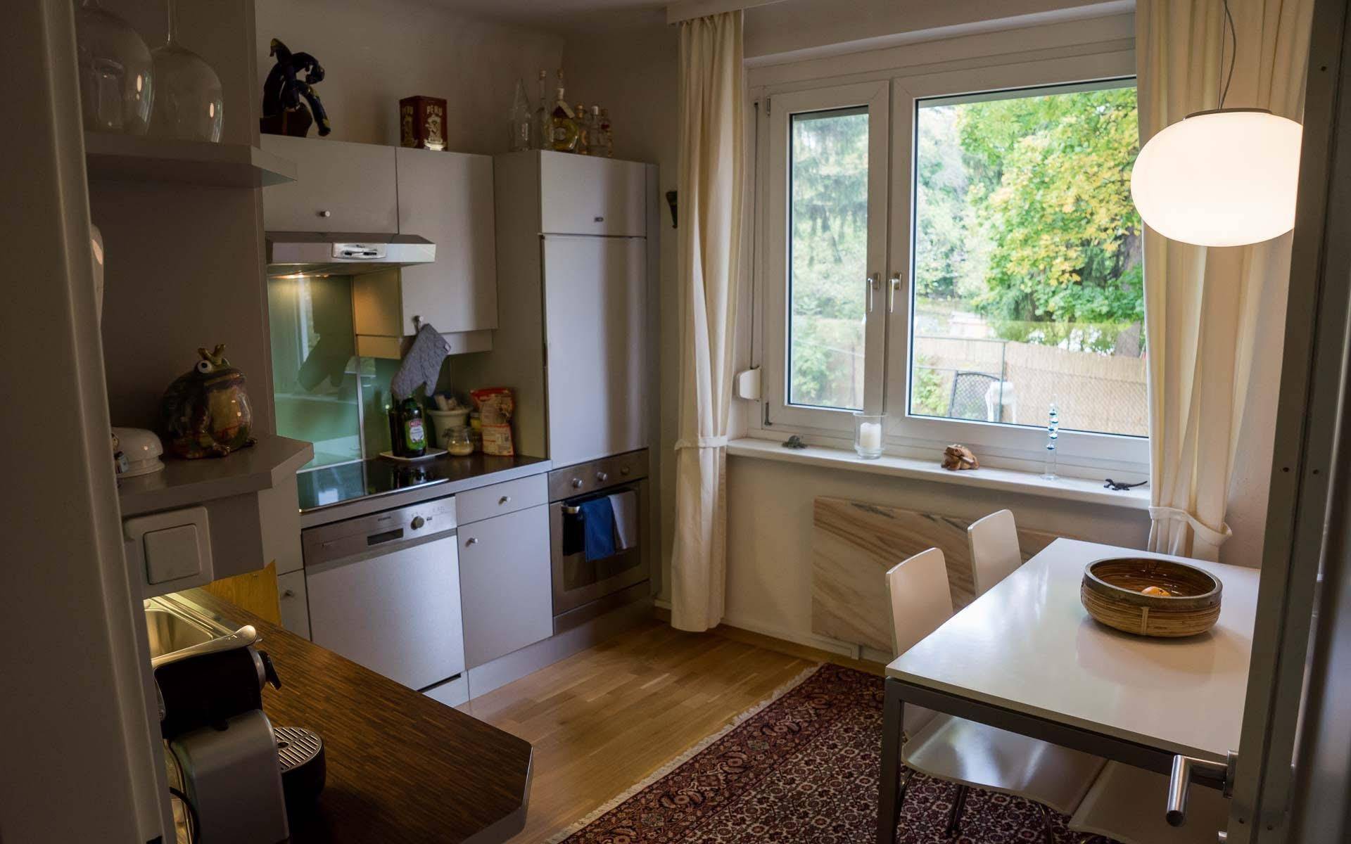Helle Küche mit weißer Einbauküche, Essbereich und Fenster mit Blick ins Grüne.