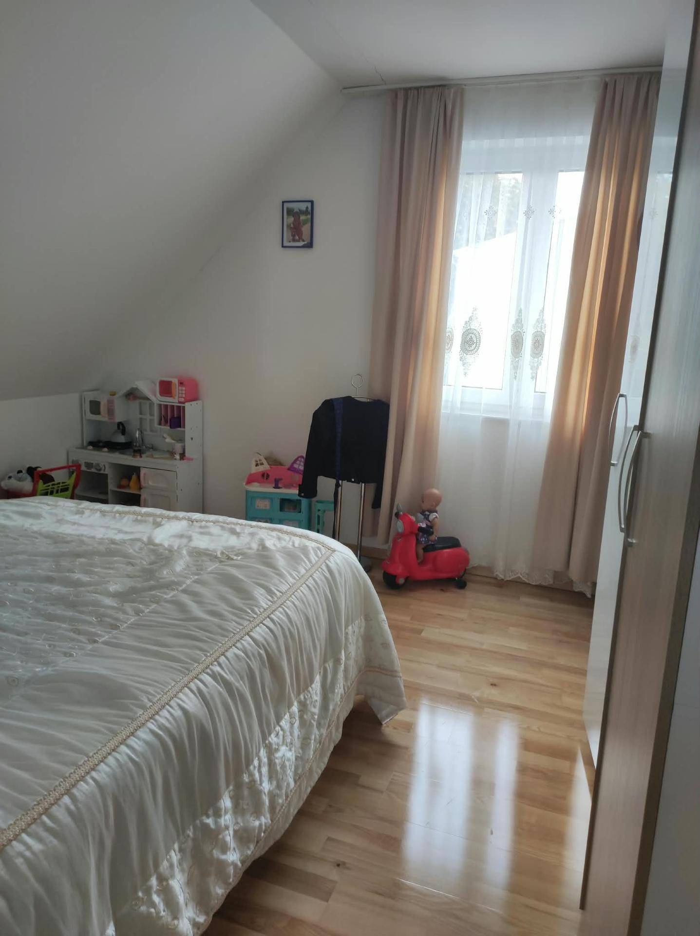 Kinderzimmer mit Bett, Holzschrank, Spielzeug und Fenster mit Vorhängen.