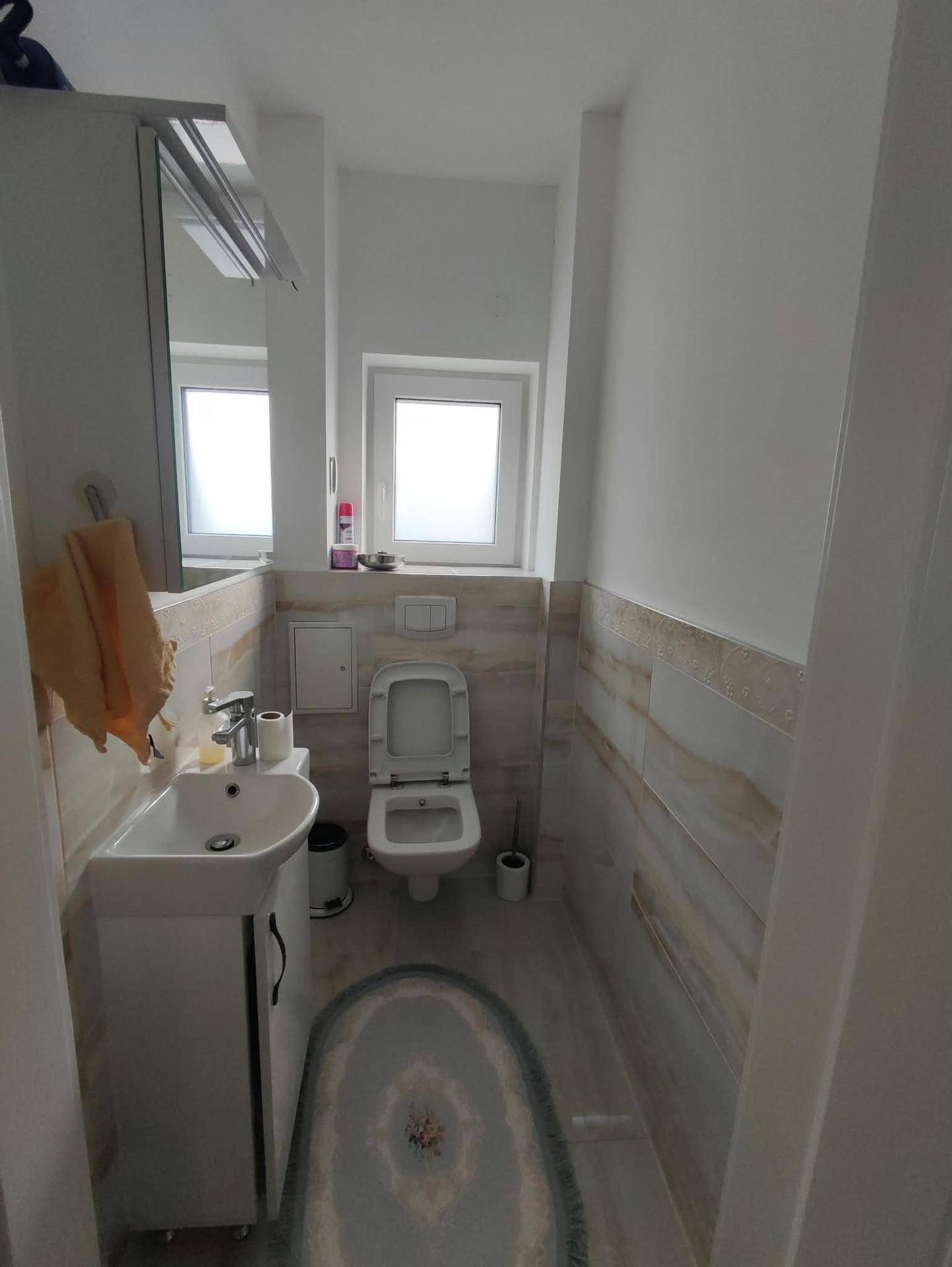 Kleines Gäste-WC mit Toilette, Waschbecken, Spiegelschrank und Fenster.