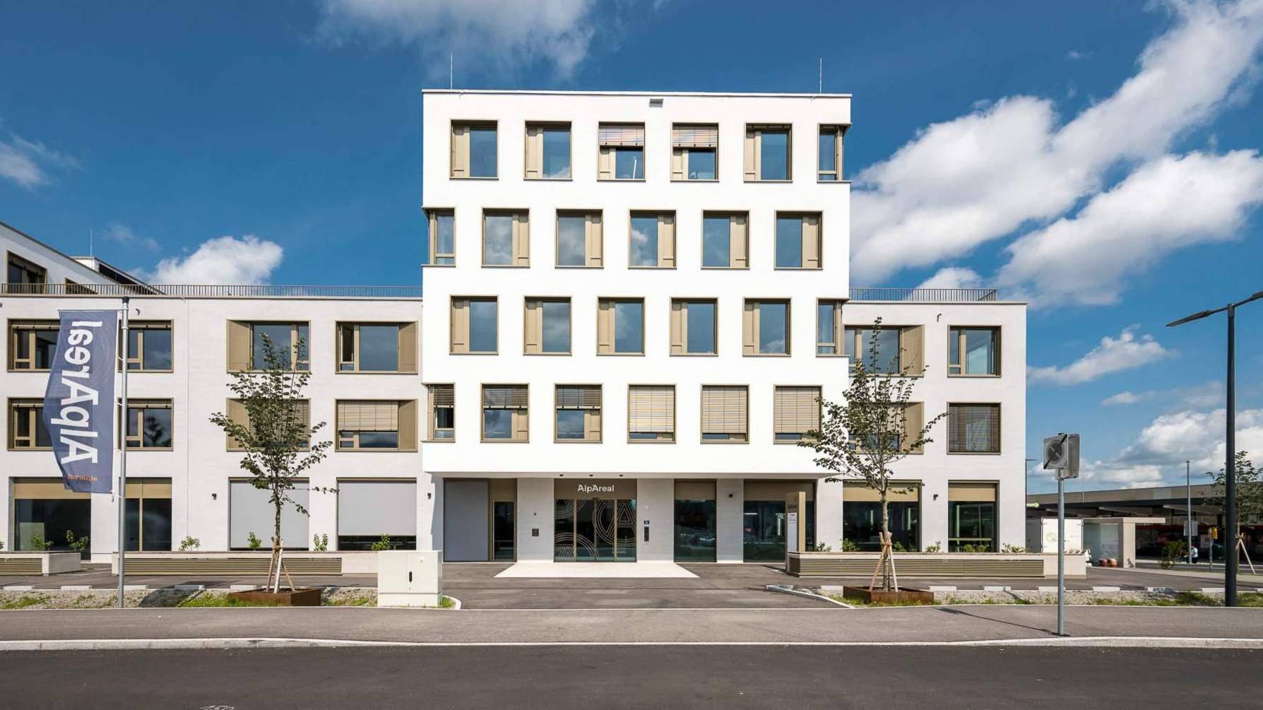 Vorderansicht eines modernen Bürogebäudes mit vielen Fenstern und Jalousien unter blauem Himmel.