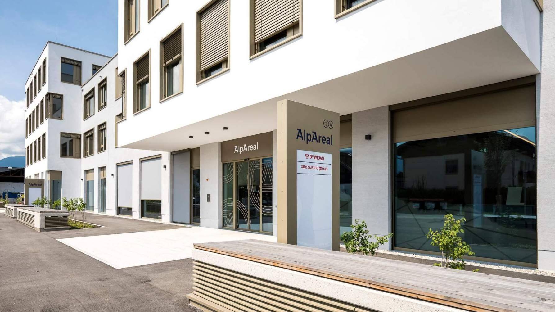 Eingangsbereich eines modernen Bürogebäudes mit Glasfronten und Beschilderung unter einem Vordach.