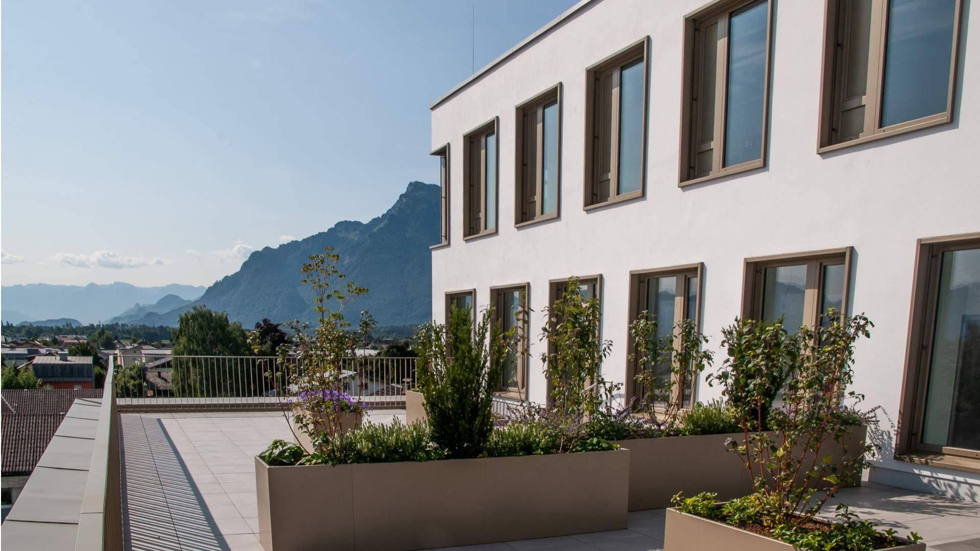 Dachterrasse mit Pflanzenkübeln und Geländer, bietet einen weiten Blick auf die umliegende Berglandschaft.