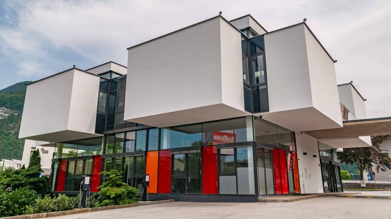 Ansicht des modernen Bürogebäudes mit Glasfassade und einer Ladestation für Elektrofahrzeuge im Vordergrund.