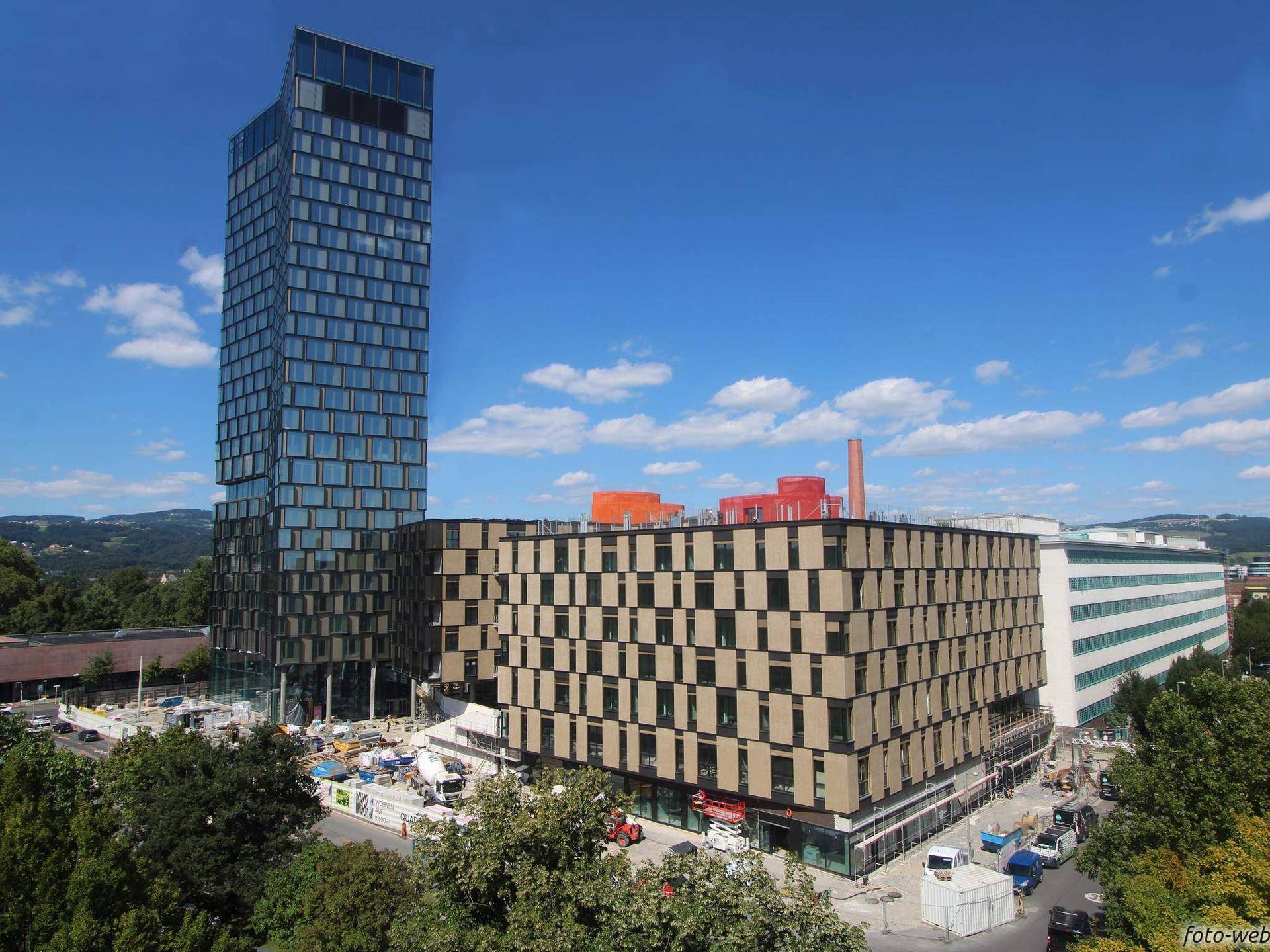 Gesamtansicht des modernen Hochhauskomplexes mit angrenzendem Gebäude unter blauem Himmel.