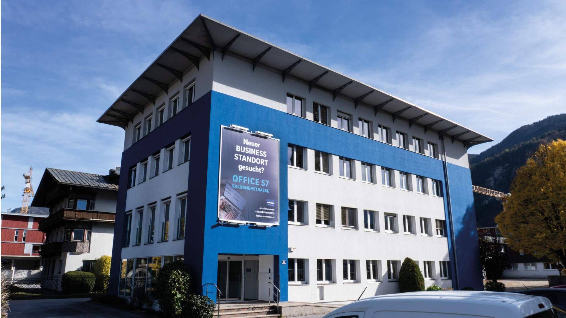 Außenansicht des modernen Bürogebäudes OFFICE 57 mit blauer Fassadenakzentuierung und Bergblick.