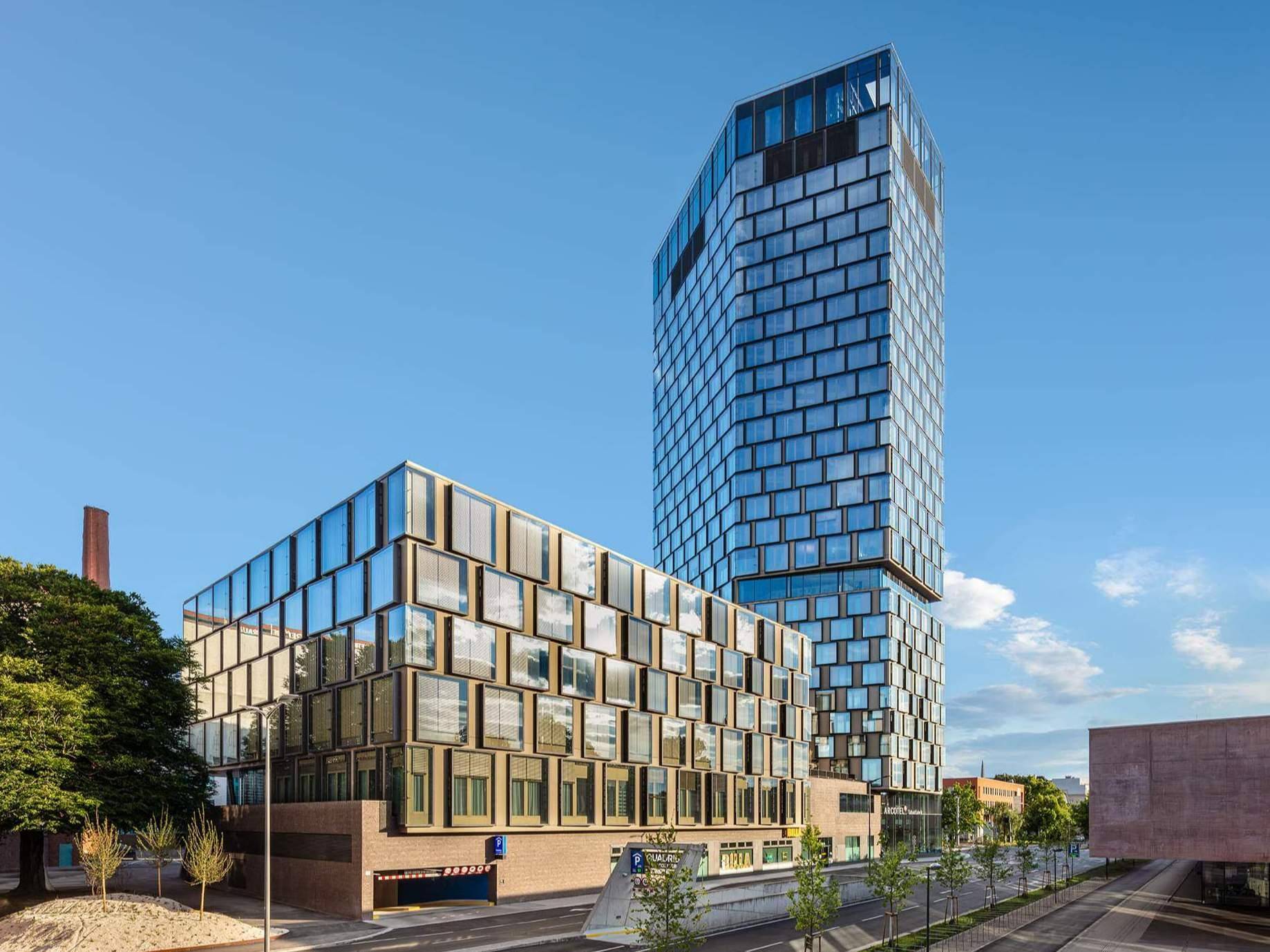 Ansicht eines modernen Bürokomplexes mit markanter Glasfassade und einem Eingang zu einer Tiefgarage.