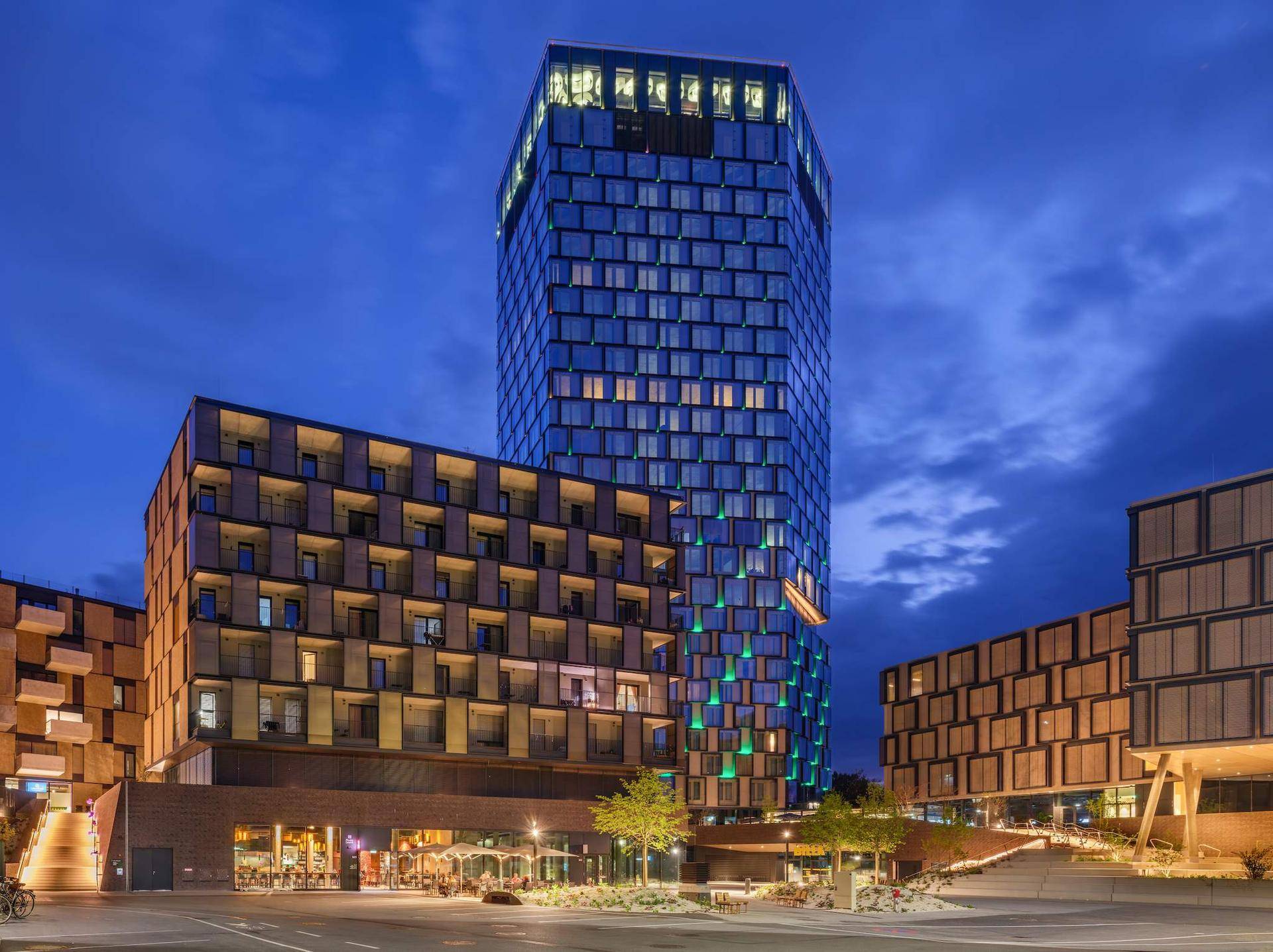 Moderne Gebäudeansicht bei Nacht mit beleuchteten Fassaden und Außenbereichen.