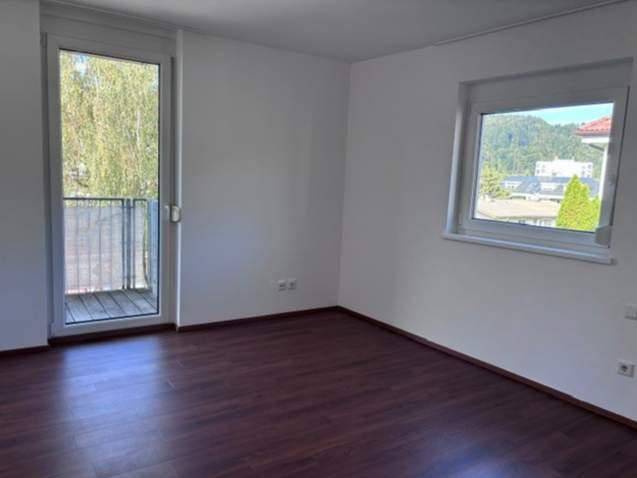 Heller Raum mit dunklem Laminatboden, Fenster und Zugang zu einem französischen Balkon.