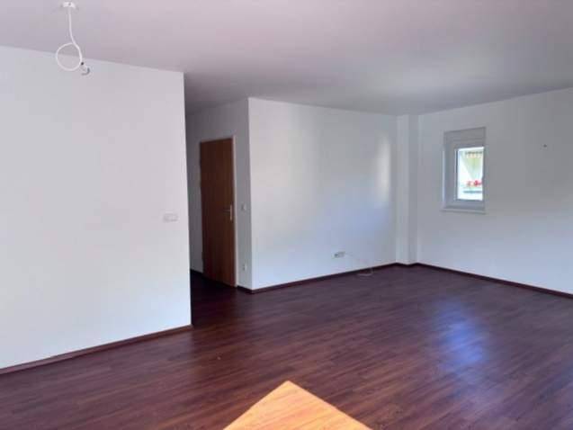 Geräumiger, unmöblierter Raum mit dunklem Laminatboden und einem Fenster für Tageslicht.