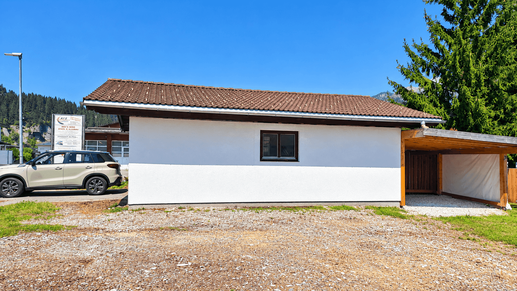 Seitenansicht eines Gebäudes mit weißer Fassade, Carport und geparktem Auto.