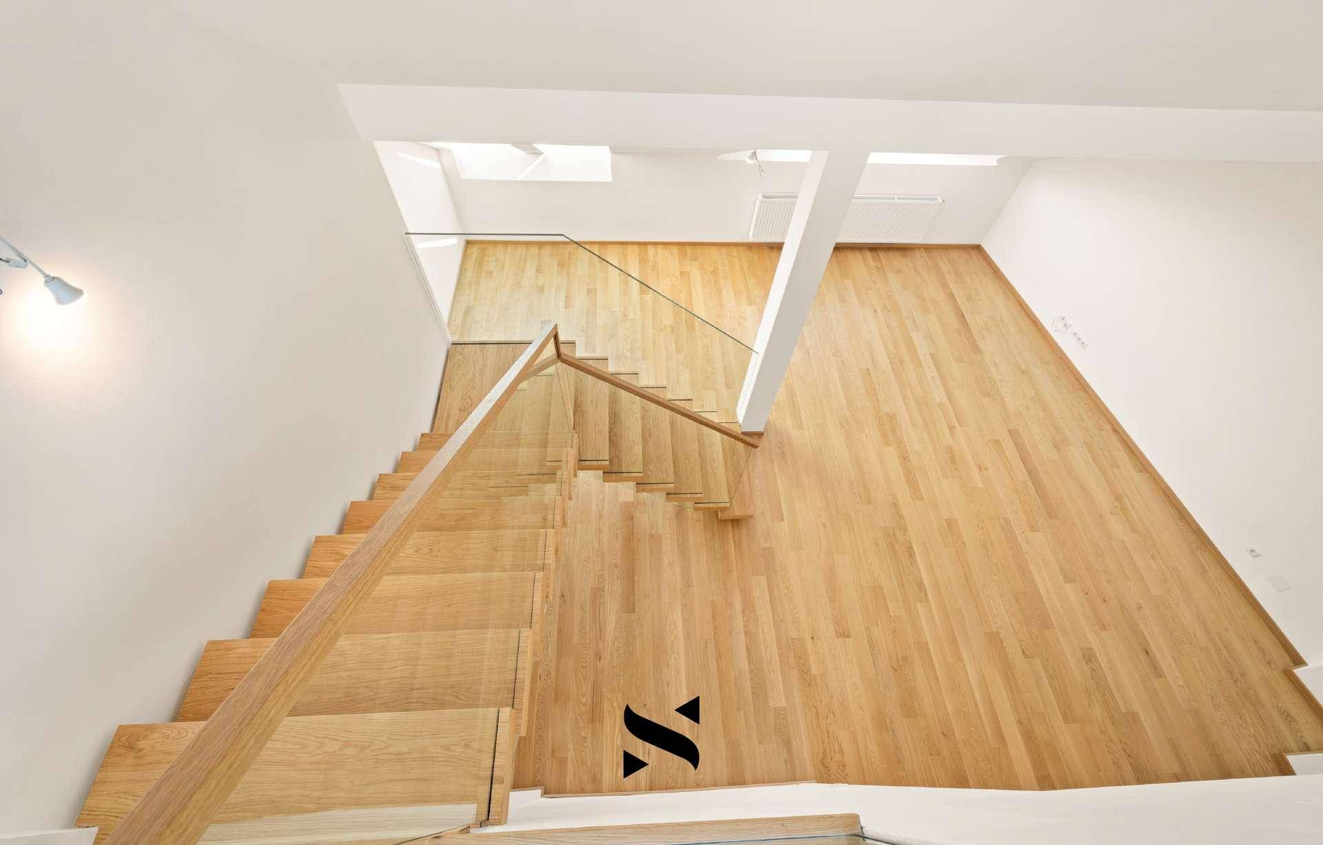 Blick von oben auf den offenen Wohnbereich mit Holzparkett und moderner Treppe.