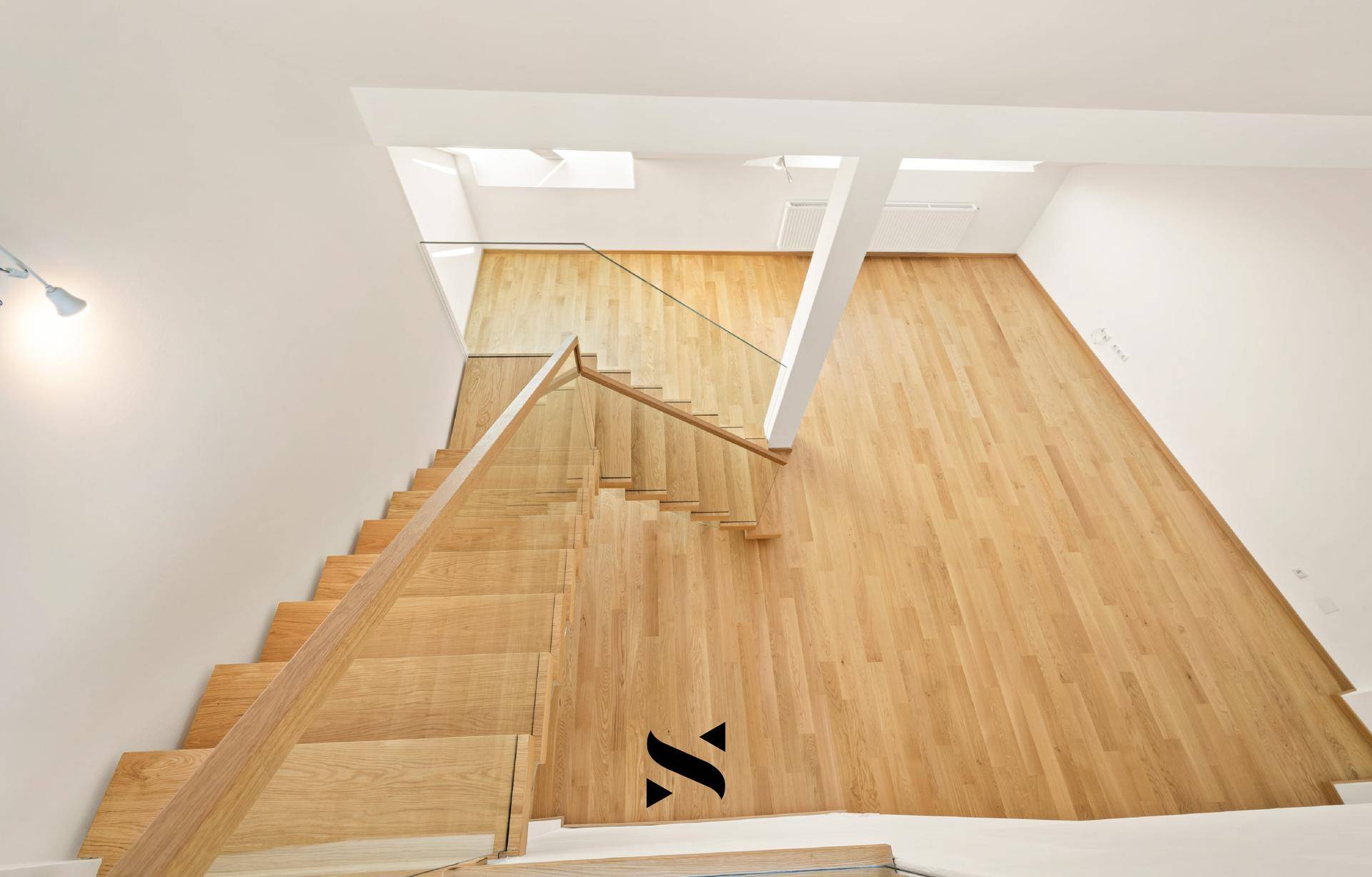 Blick von der Treppe auf den offenen Wohnbereich mit hellem Parkettboden und viel Tageslicht.
