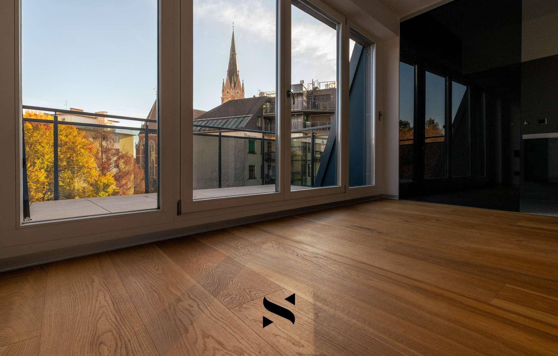 Helles Zimmer mit Holzboden, großen Fenstern und Zugang zu einem Balkon mit Aussicht.