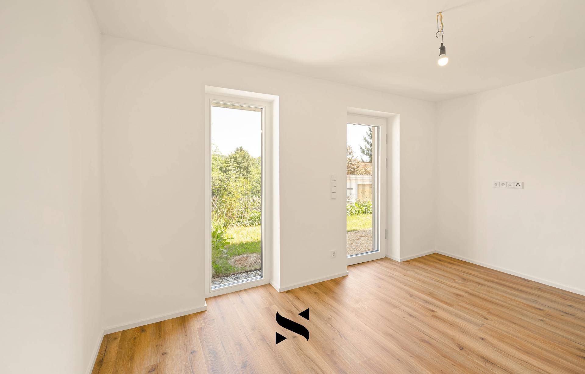 Lichtdurchfluteter Raum mit Laminatboden und Fenstern, die einen Blick ins Grüne ermöglichen.